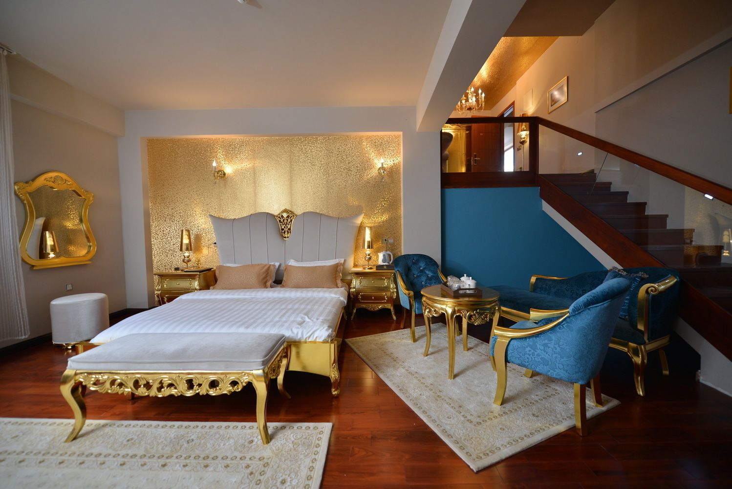 Ein luxuriöses Schlafzimmer mit einem großen Bett, einem goldenen Kopfteil, einem blauen Sessel und einer Treppe.