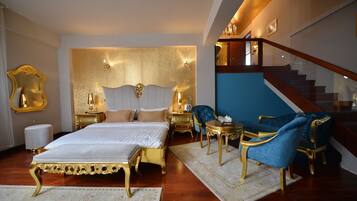 Ein luxuriöses Schlafzimmer mit einem großen Bett, einem goldenen Kopfteil, einem blauen Sessel und einer Treppe.