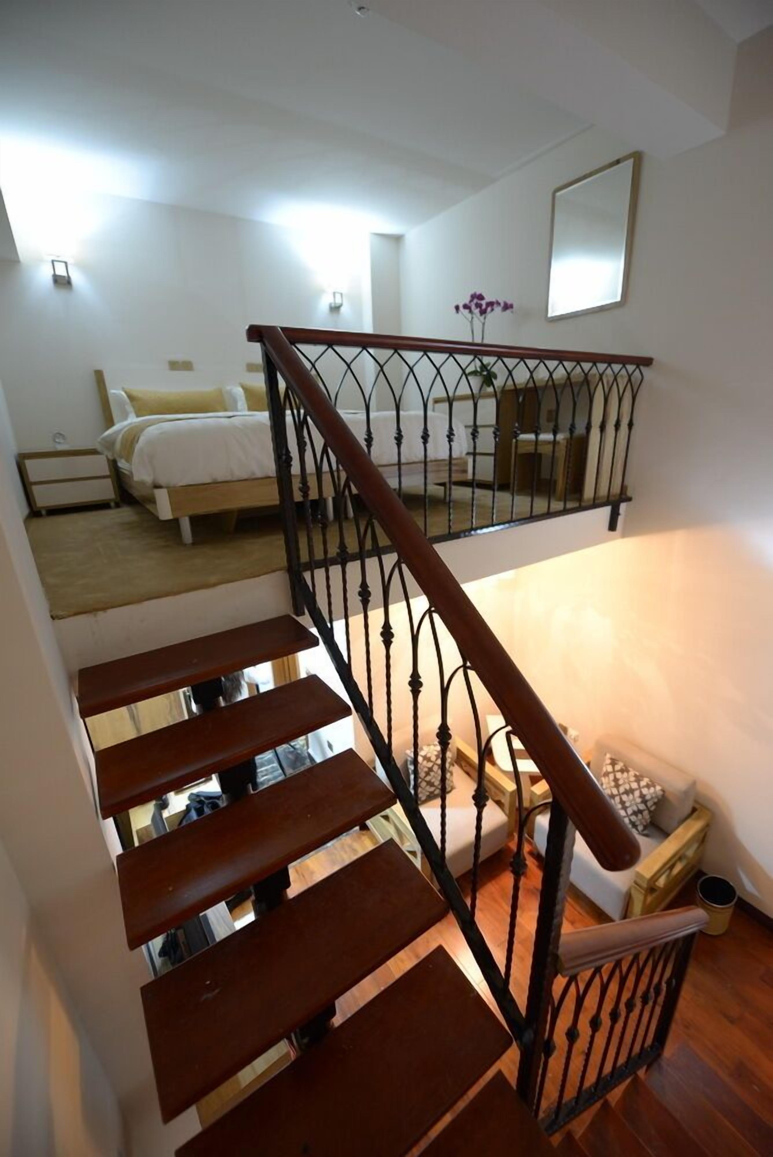 Un escalier avec des marches en bois et une rampe en métal menant à une chambre à coucher équipée d’un lit et d’une table de chevet.