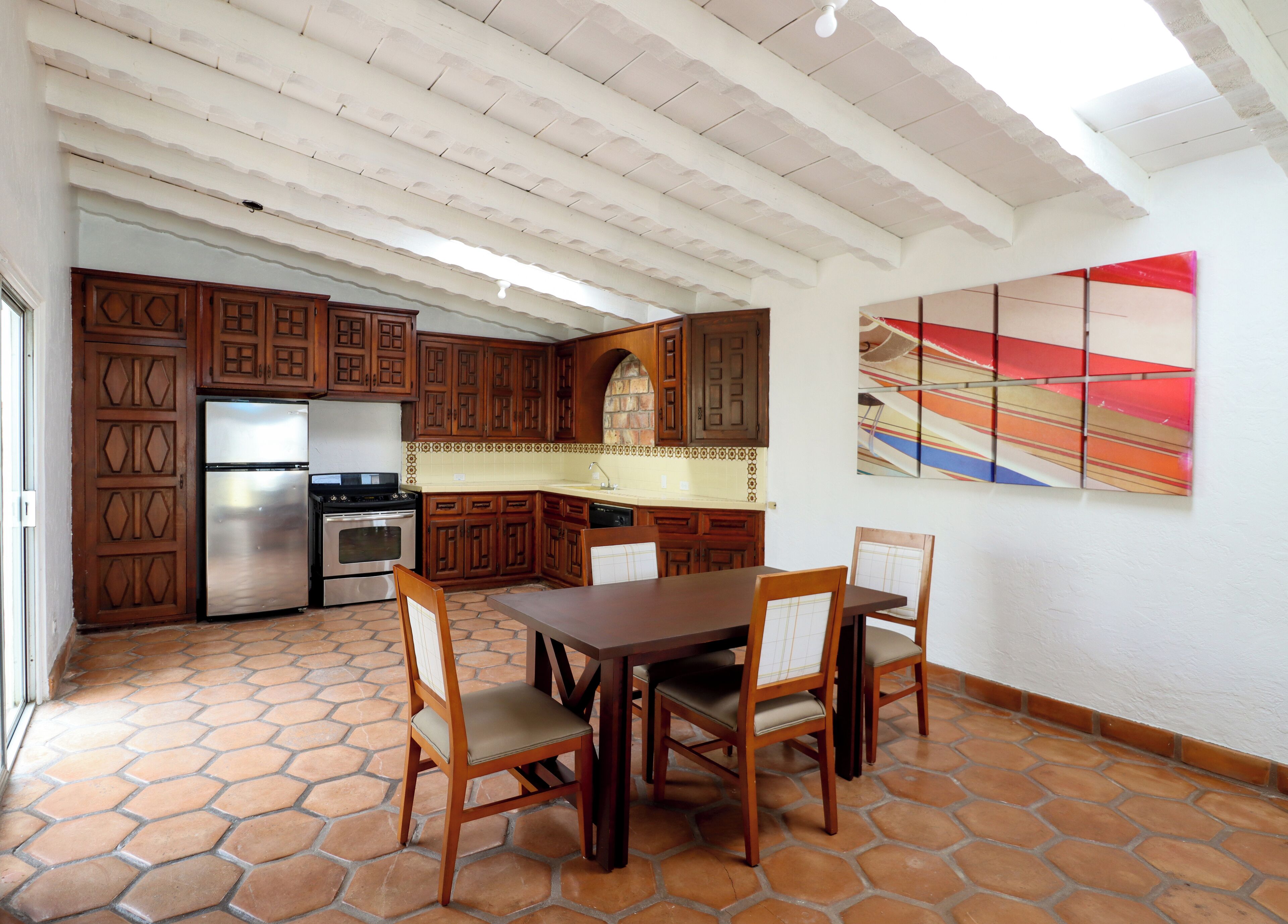 A kitchen with wooden cabinets, a stainless steel refrigerator, a stove, and a dining table with chairs.