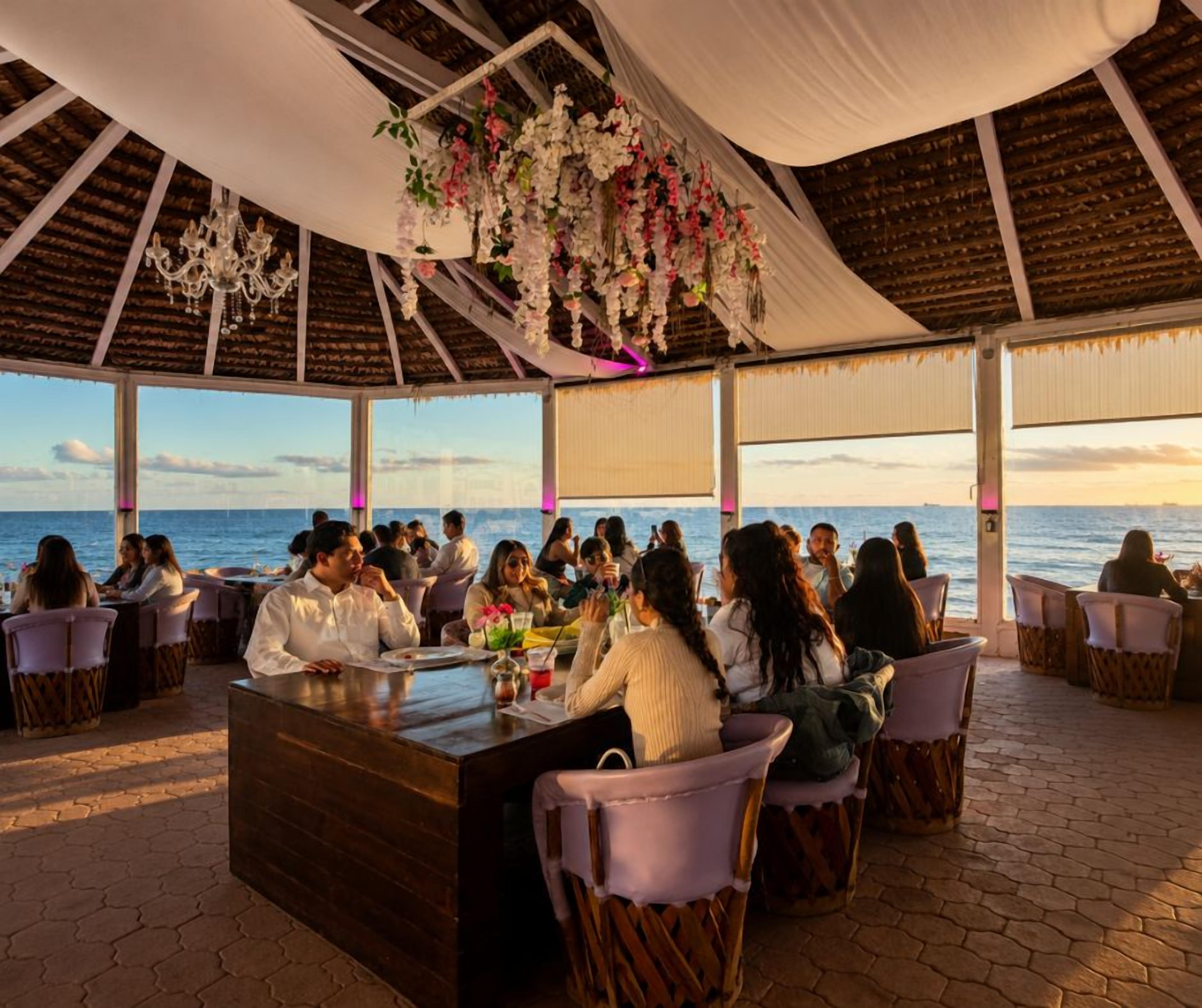 An outdoor dining area with a view of the sea, featuring a wooden reception desk and wicker chairs.