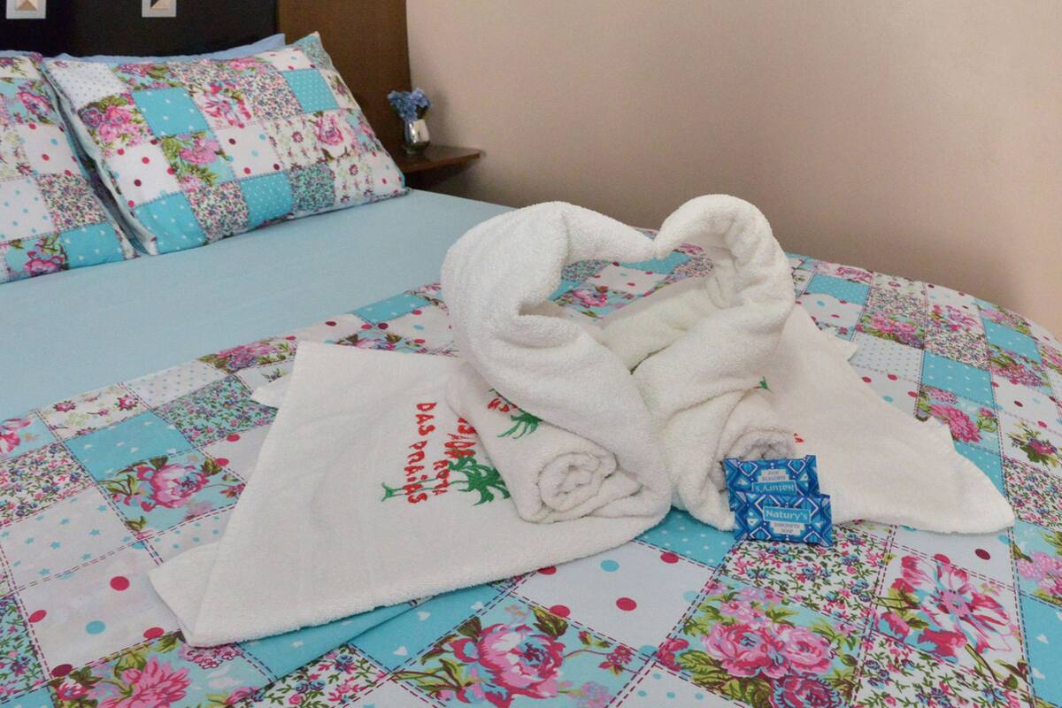 Una cama bien hecha con colcha floral, una toalla blanca y un objeto azul pequeño sobre la cama.