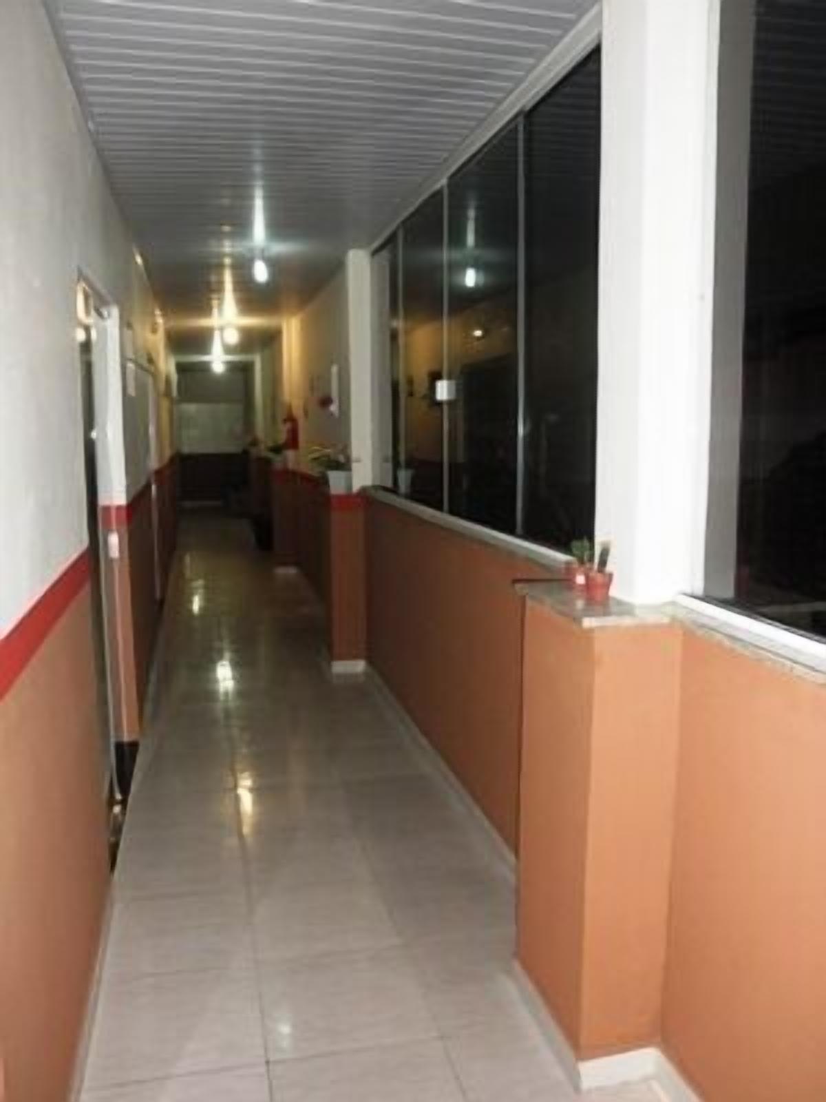 A long, narrow hallway with a tiled floor and a ceiling with a grid pattern. There are windows on one side and a door on the other.