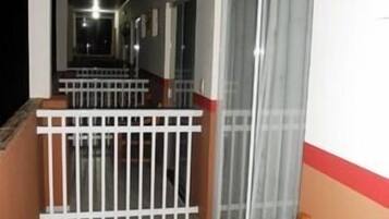Corredor com um banco de madeira, corrimão branco e porta de vidro.