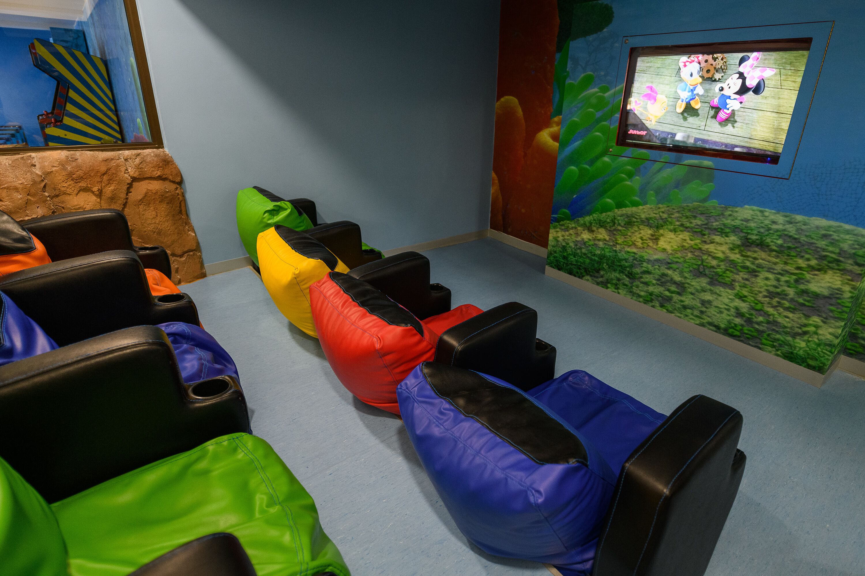 Une pièce dotée de fauteuils en forme de sacs de haricots aux couleurs vives, d’un écran de télévision diffusant des dessins animés et d’une fresque murale aux tons bleus et verts.