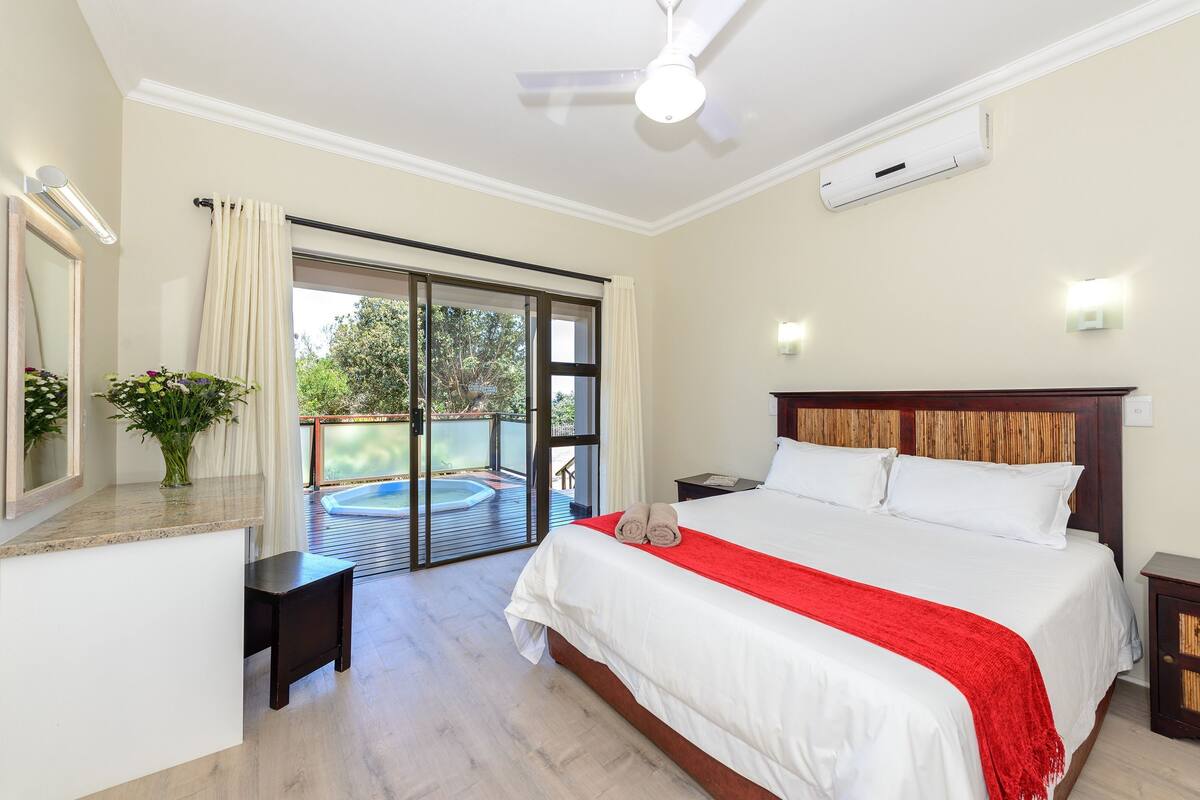 A hotel room with a bed, a small table, a nightstand, a ceiling fan, and a sliding glass door leading to an outdoor area.