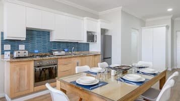 A modern kitchen with white cabinets, a blue backsplash, and a dining area with a glass table set for four.