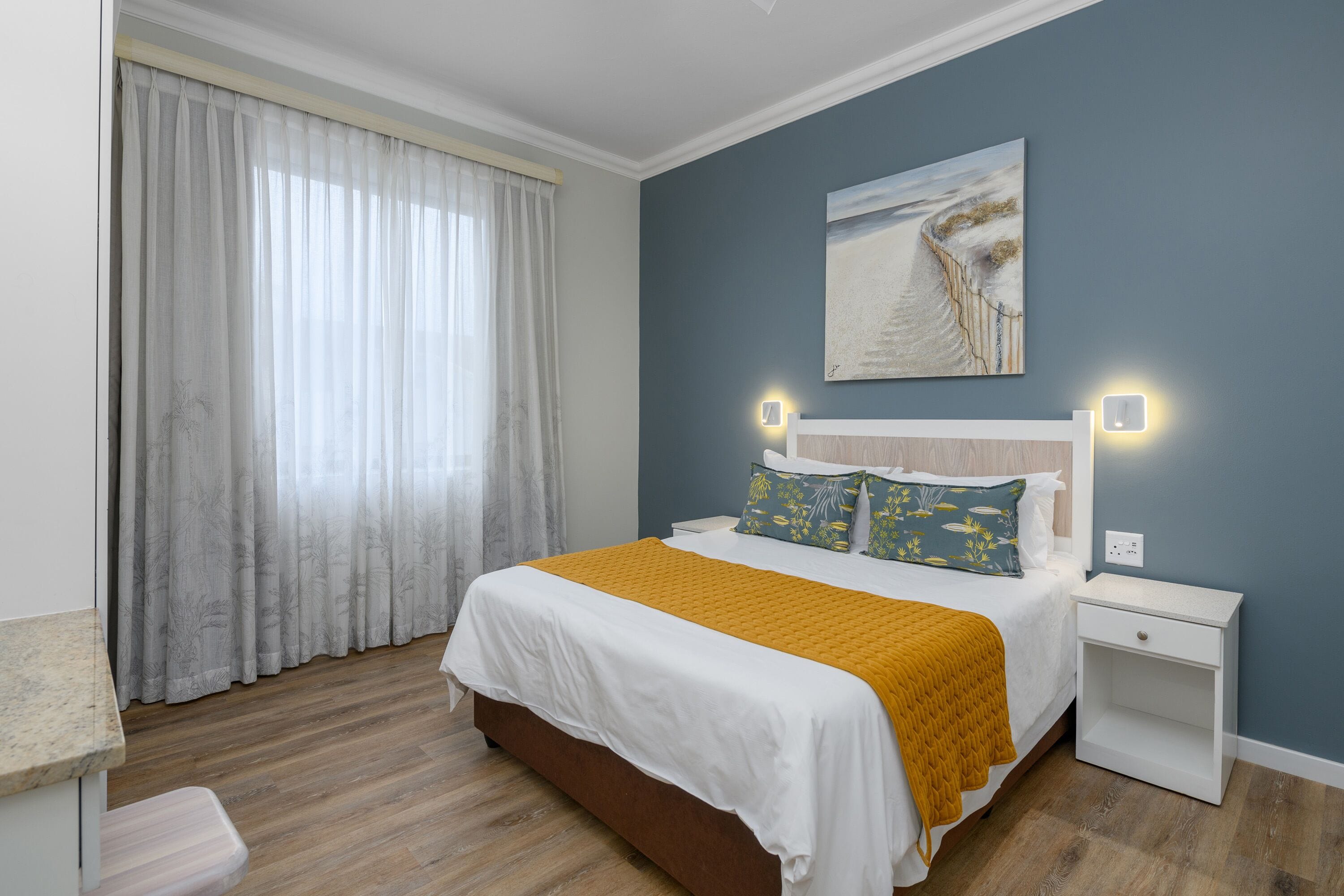 Un dormitorio con cama, mesitas de noche, una ventana con cortinas y un cuadro en la pared.