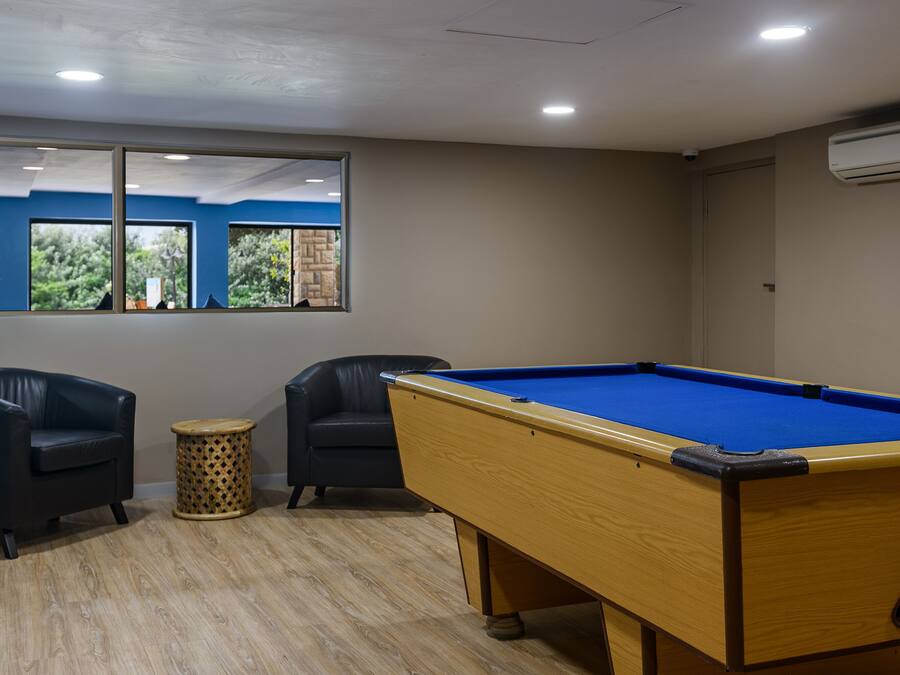A pool table with two chairs, a small round table, and a window with a view of greenery.