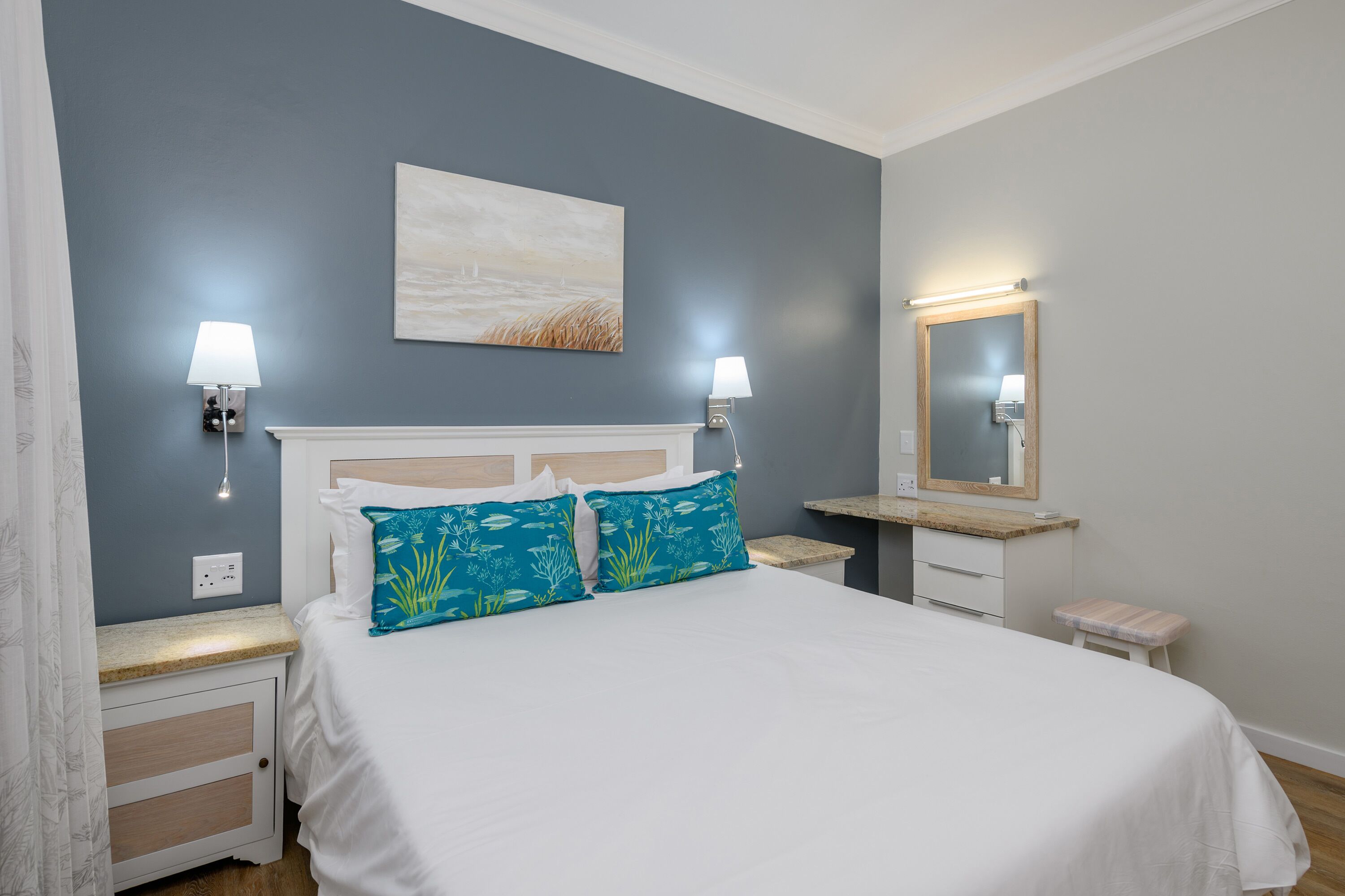 A bedroom with a bed, nightstands, a mirror, and a painting on the wall.