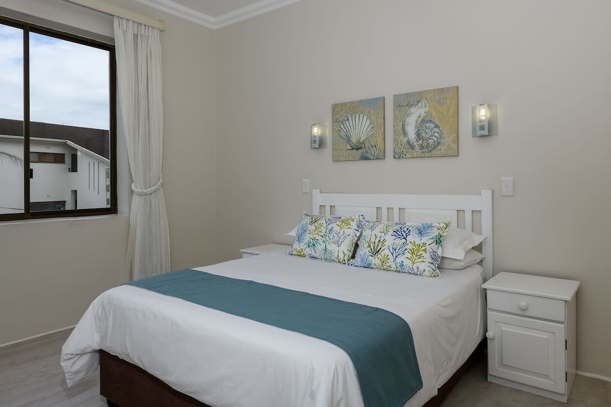 A bedroom with a bed, nightstand, and artwork on the wall.