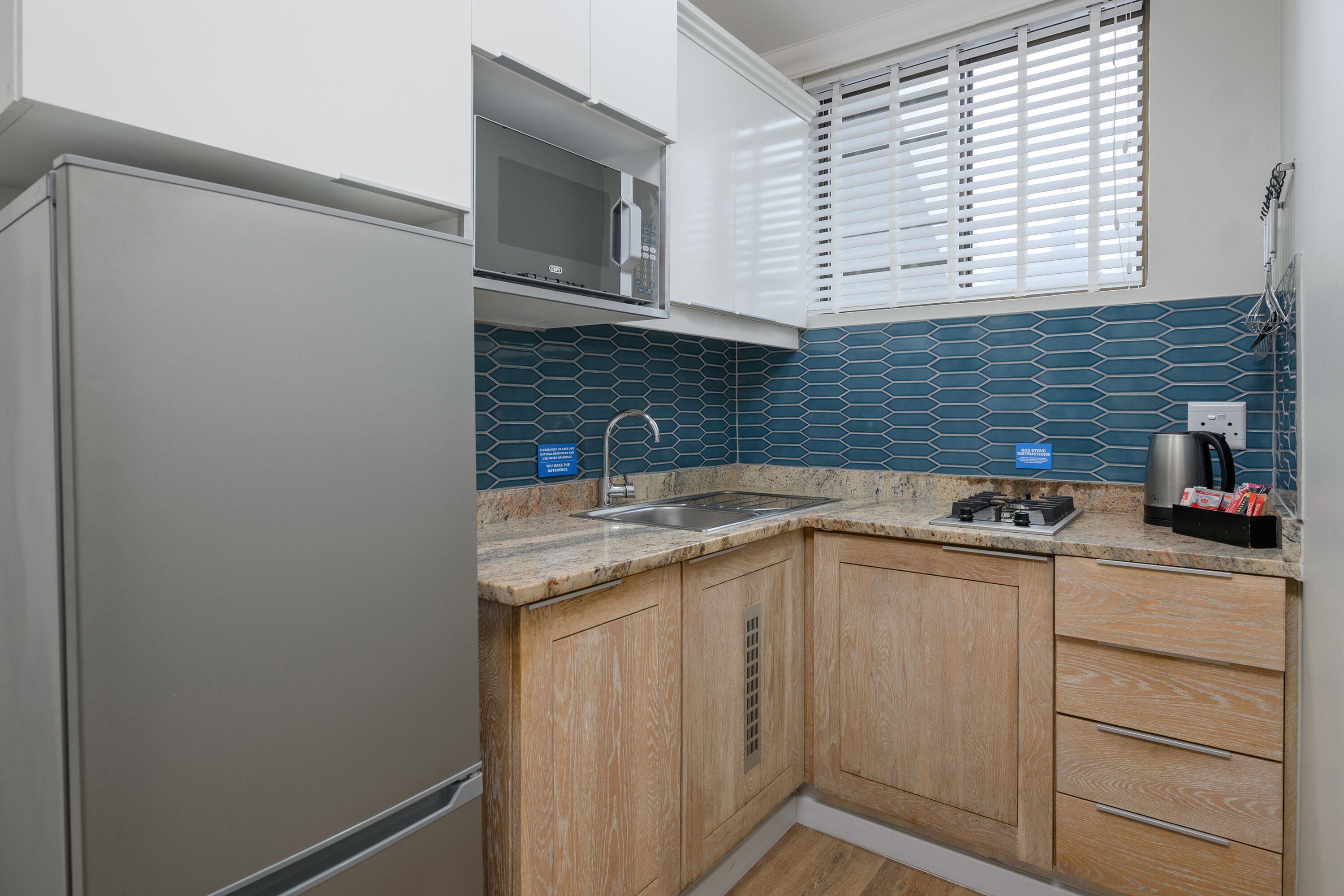 A compact kitchen with a stainless steel refrigerator, a microwave, a sink, and wooden cabinets.