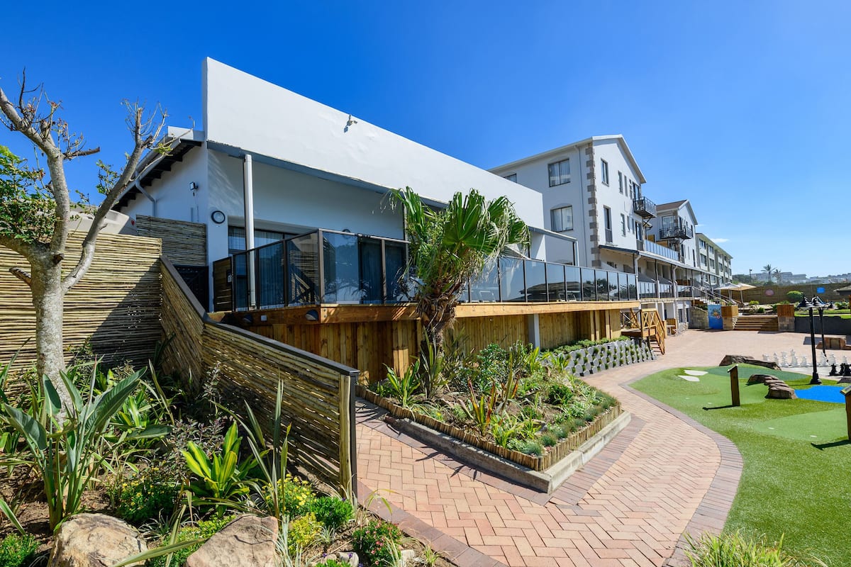 A modern hotel with a flat roof, large windows, and a landscaped garden with pathways and plants.