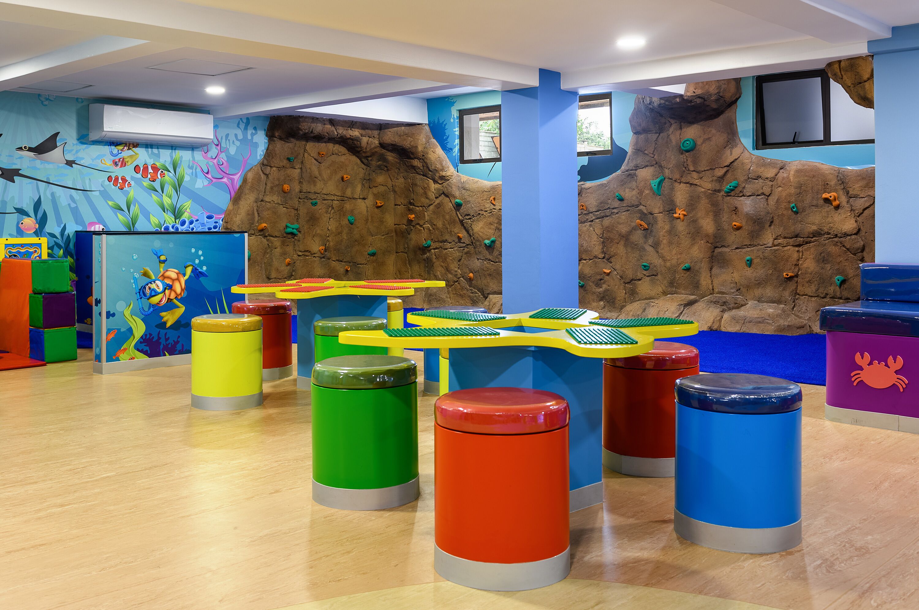 A children's play area with climbing walls, colorful stools, and a mural of an underwater scene.