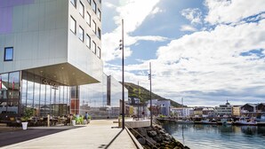 Un edificio moderno con fachada de vidrio, una terraza de madera y un puerto deportivo con barcos.