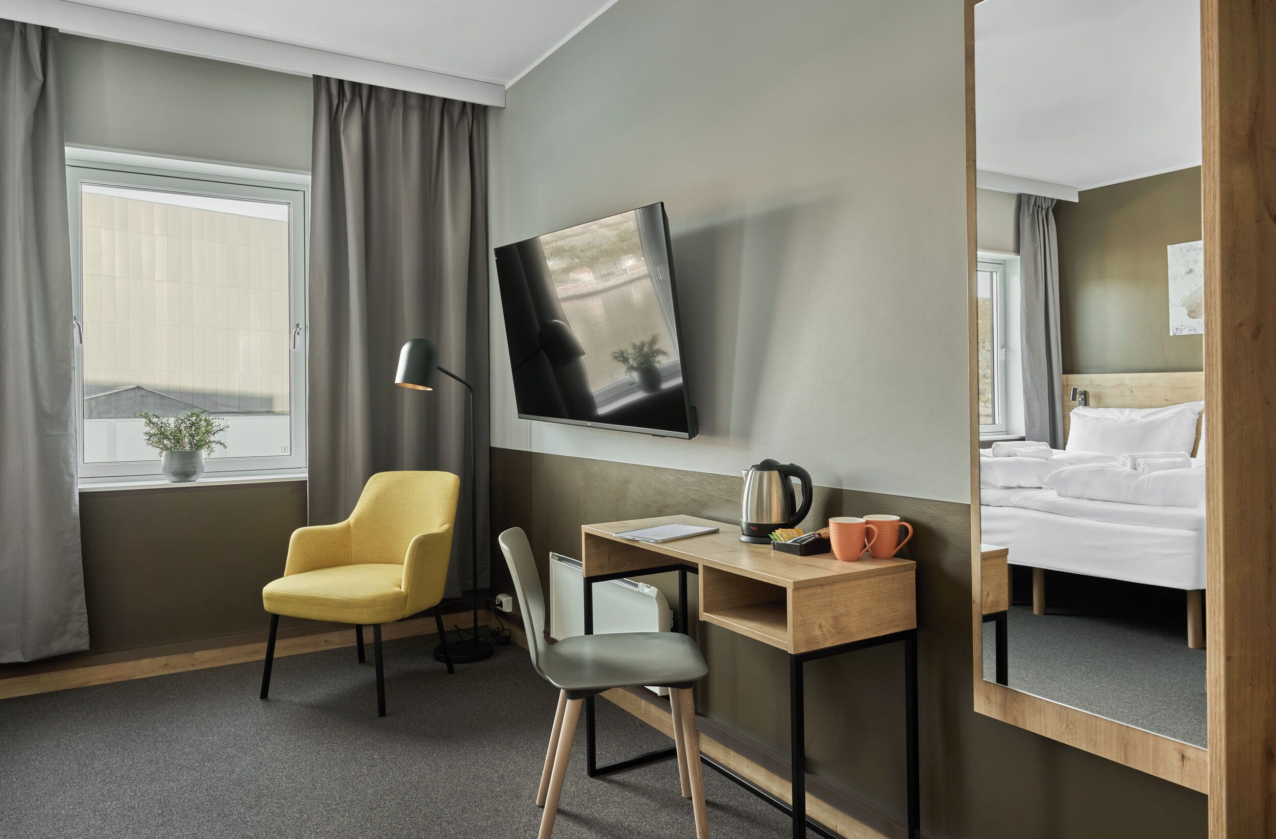 Una habitación de hotel con cama, escritorio con silla, televisor y ventana con cortinas.