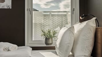 Ein Schlafzimmer mit einem Bett, Kissen, einer Nachttischlampe, einem Fenster mit Blick auf einen Zaun und einer Topfpflanze.