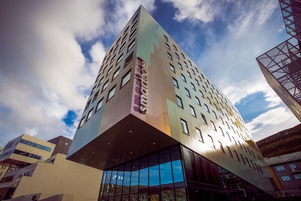 A modern building with a unique angular design, featuring a prominent entrance with glass doors and a visible name sign. - Smarthotel Hammerfest (Hammerfest)