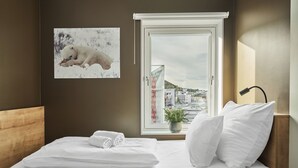 A hotel room with a bed, a window with a city view, a wall-mounted picture of a dog, and a bedside lamp. - Smarthotel Hammerfest (Hammerfest)