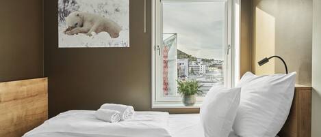 A hotel room with a bed, a window with a city view, a wall-mounted picture of a dog, and a bedside lamp.