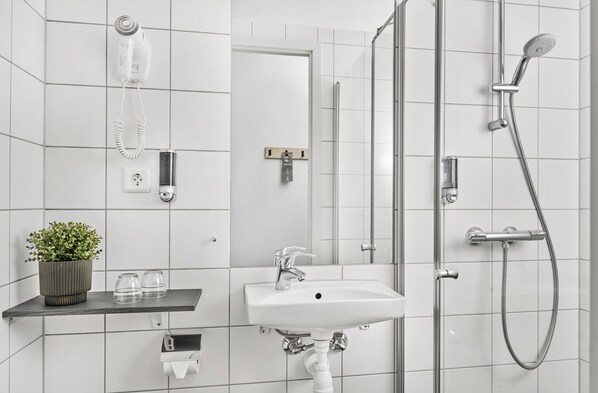 Un baño moderno con ducha, lavamanos y secador de pelo montado en la pared.