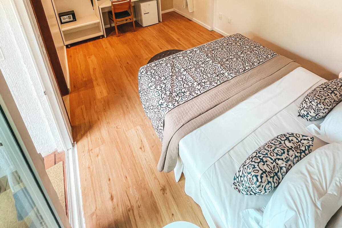 Quarto de hotel com cama, escrivaninha com computador, televisão e guarda-roupa.