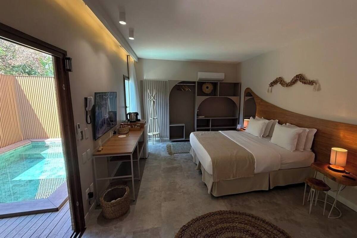 Quarto com cama, mesas de cabeceira, escrivaninha e vista para uma piscina ao ar livre.