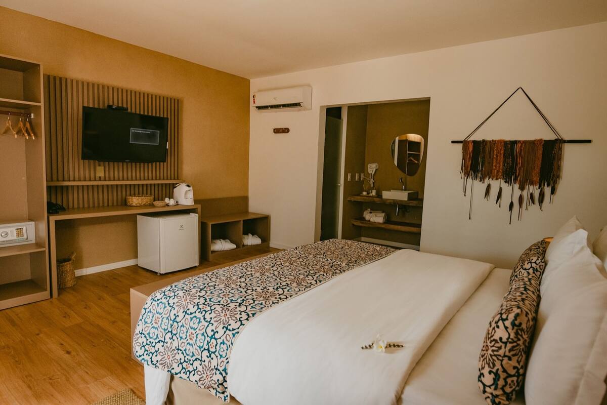 Quarto de hotel moderno com uma cama grande, televisão, mini-geladeira e guarda-roupa.