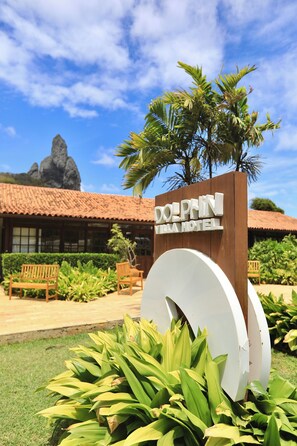 Señal del Hotel Dolphin Villa, con un jardín tropical y una montaña al fondo.