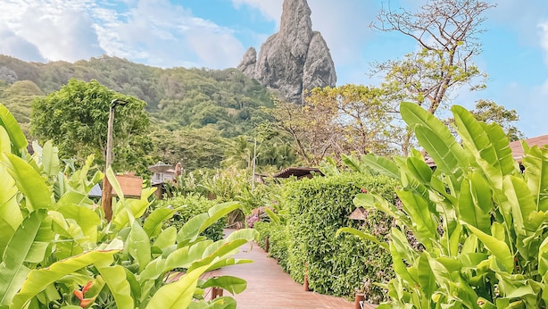A wooden pathway leading to a mountain peak, surrounded by lush greenery and a clear sky.