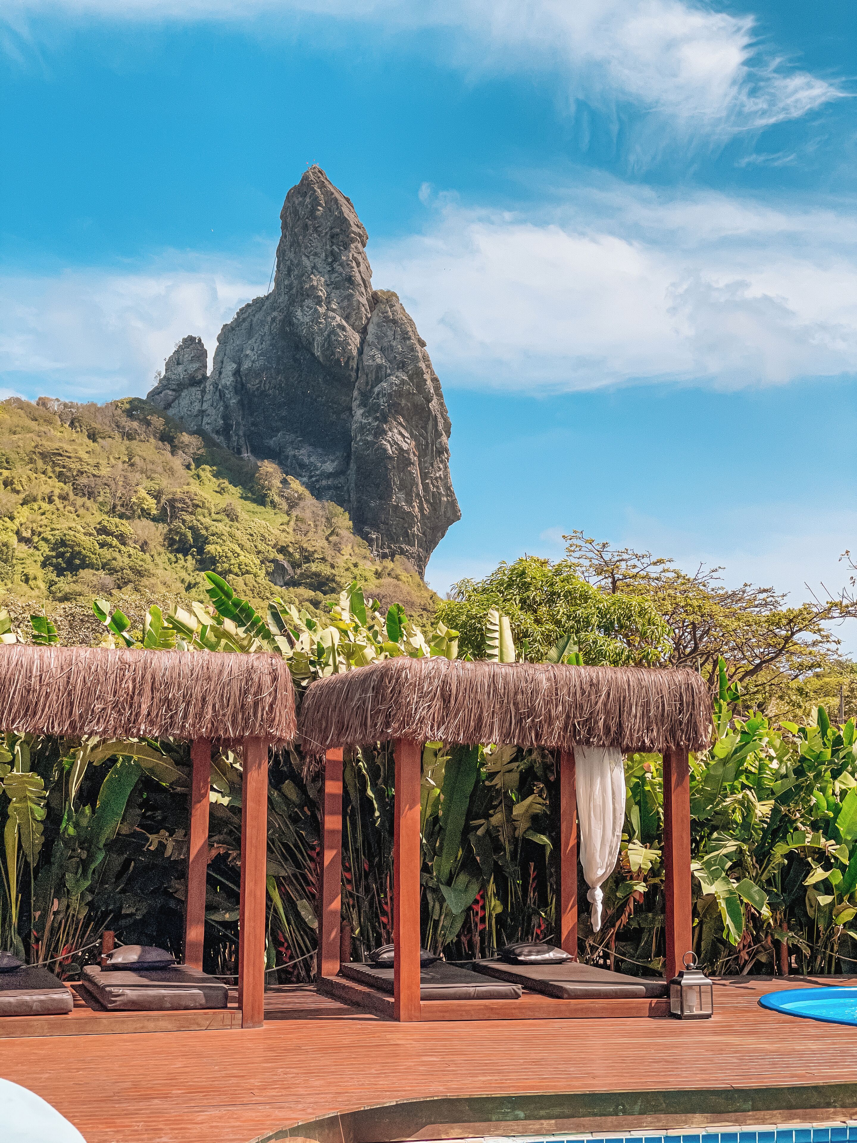 A poolside area with thatched umbrellas, lounge chairs, and a view of a rocky mountain.