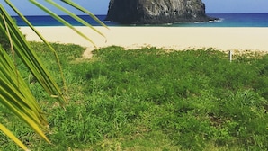 A beach with a prominent rock formation, clear blue sky, and lush greenery.