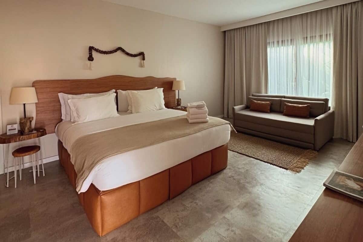 Quarto de hotel com uma cama grande, um sofá, uma mesa pequena e uma janela com cortinas.