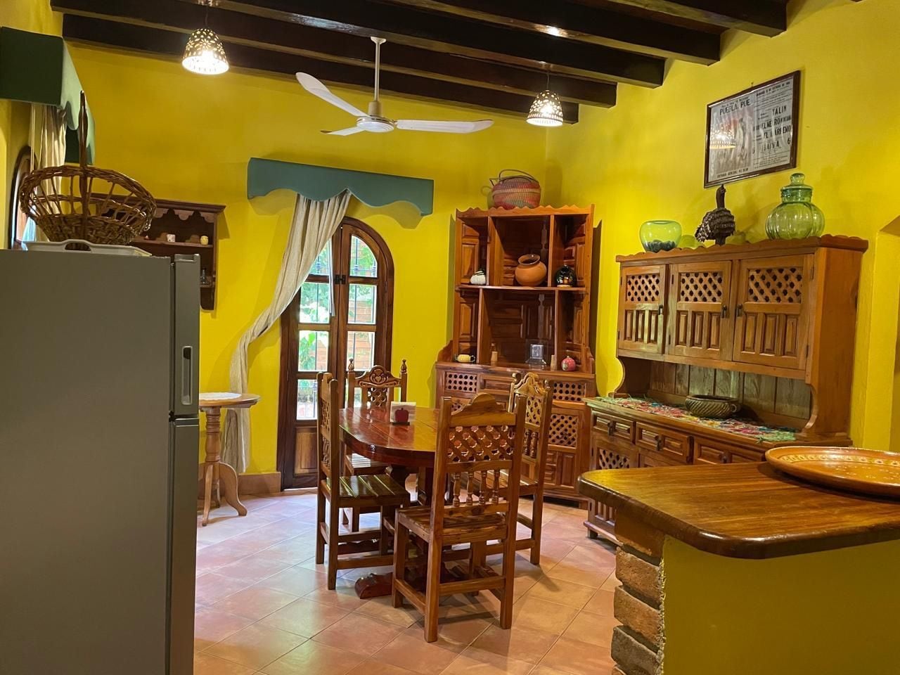 Una cocina con armarios de madera, una mesa de comedor, sillas y un refrigerador.