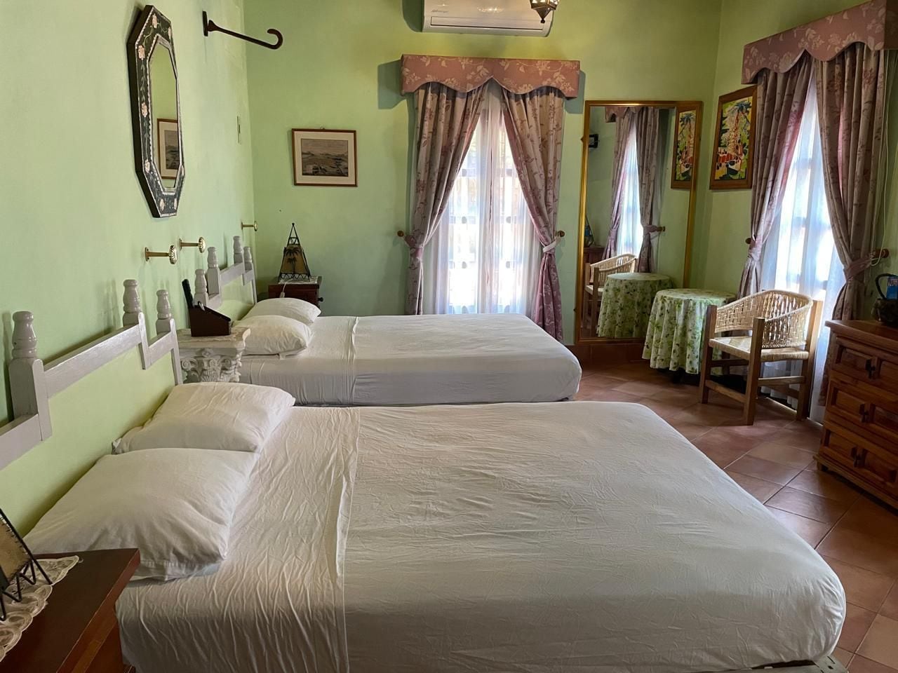 A room with two beds, a wooden dresser, a chair, and a wall-mounted air conditioner.