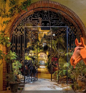 An ornate wrought iron gate with a brick archway leading to a lush garden. - Hotel Suites La Hacienda (Puerto Escondido)