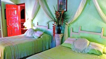 Una habitación con dos camas, una puerta roja, una mesita de noche con una lámpara y un cuadro en la pared.