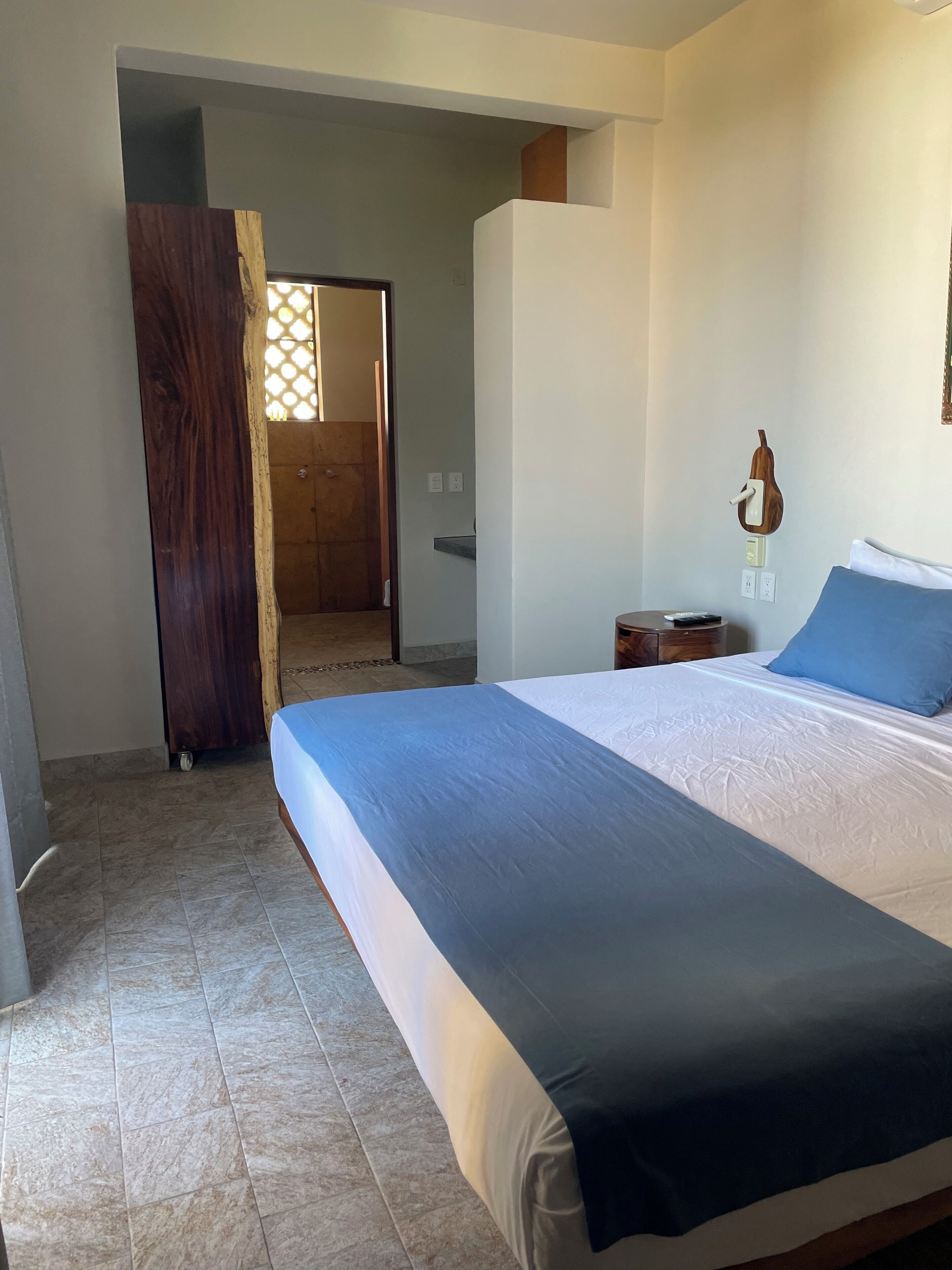 Un dormitorio con una cama grande, una puerta de madera, una mesita de noche pequeña y una guitarra colgada en la pared.