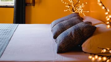 Una cama con ropa de cama blanca y dos almohadas estampadas, una ventana con vistas a la vegetación y un detalle de madera en la pared.