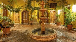 Une cour intérieure avec une fontaine centrale, des plantes en pot et des murs jaunes.
