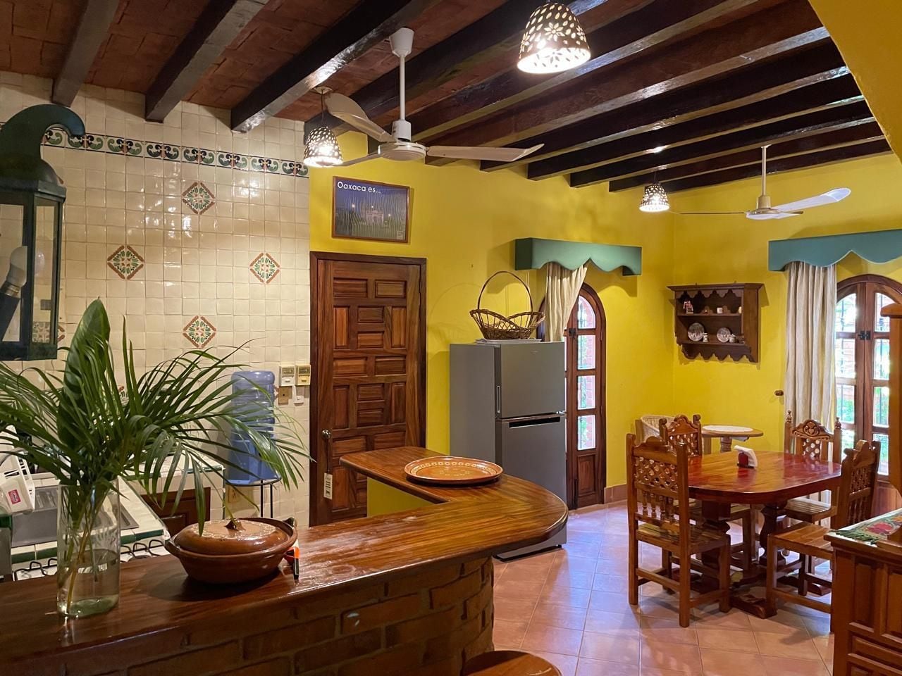 A kitchen with a wooden counter, a refrigerator, and a dining area with chairs and a table.