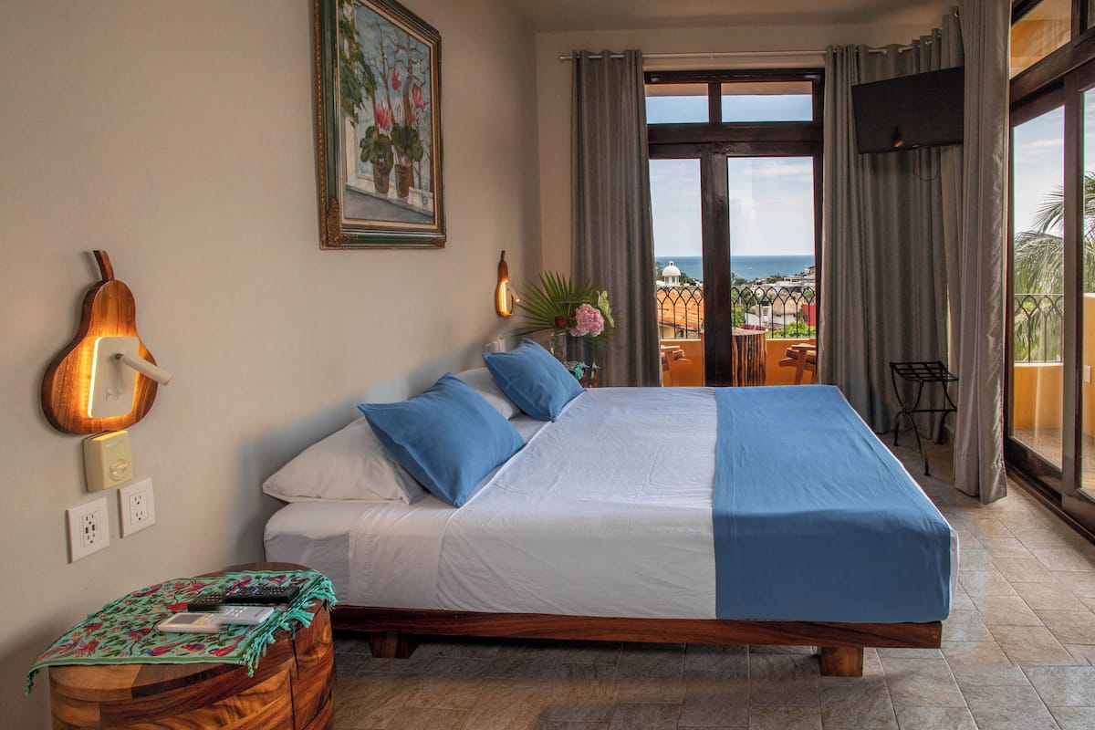Une chambre avec un grand lit, un ventilateur de plafond, une télévision et une vue sur la mer.