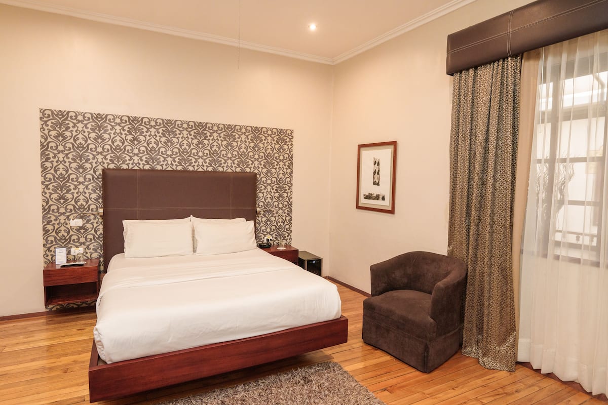 Une chambre à coucher avec un grand lit, une table de chevet, une chaise et un papier peint à motifs.