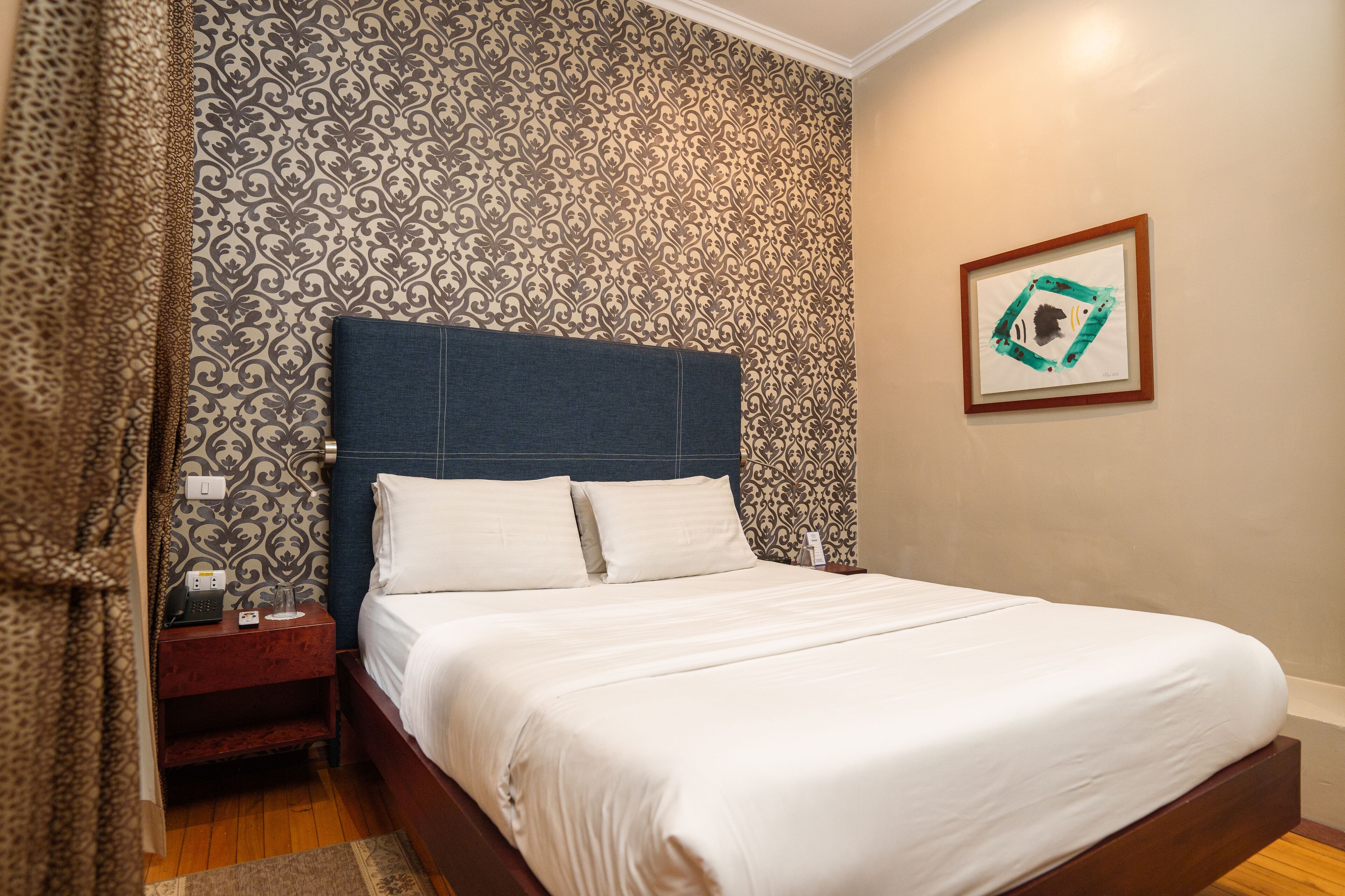 Una cama bien tendida con sábanas blancas, cabecera de madera y papel tapiz estampado.