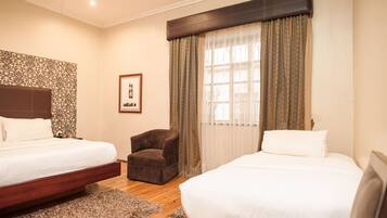 Habitación de hotel con dos camas, un sillón marrón, un cabecero estampado y un cuadro en la pared.