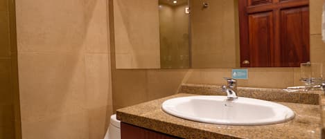 Un baño con lavamanos blanco, encimera de granito, armarios de madera y un espejo grande.