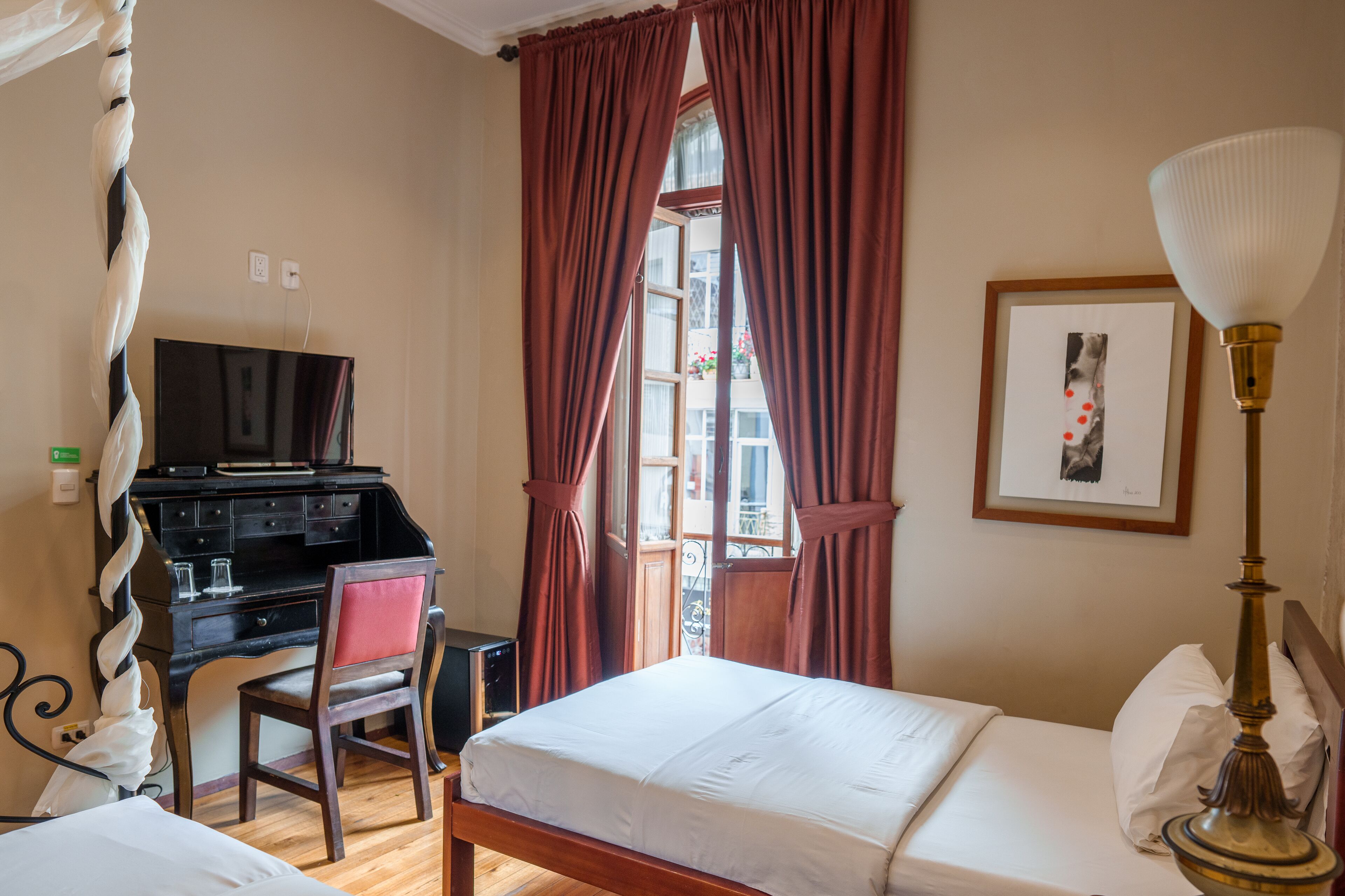Una habitación de hotel con cama, escritorio con silla, televisor y ventana con cortinas.