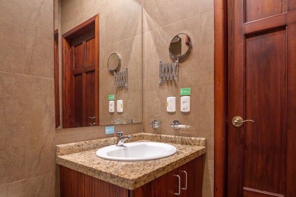 Un baño con lavamanos de encimera de granito, armarios de madera, un espejo y una puerta.