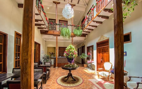 A spacious lobby with a high ceiling, a central round table with a floral arrangement, and a staircase with wooden railings.