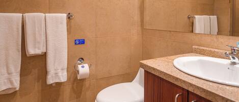 Un baño con inodoro, lavamanos y toallas colgadas en la pared.